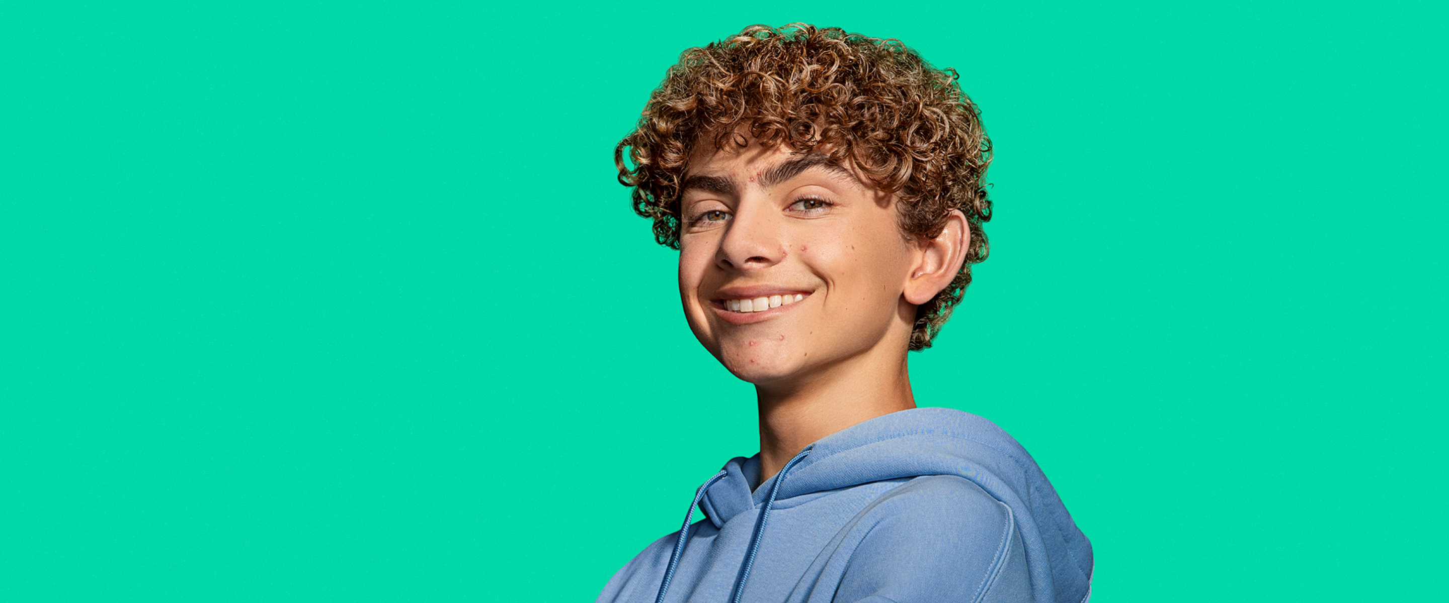 Young male teen with visible acne smiling confidently towards camera.