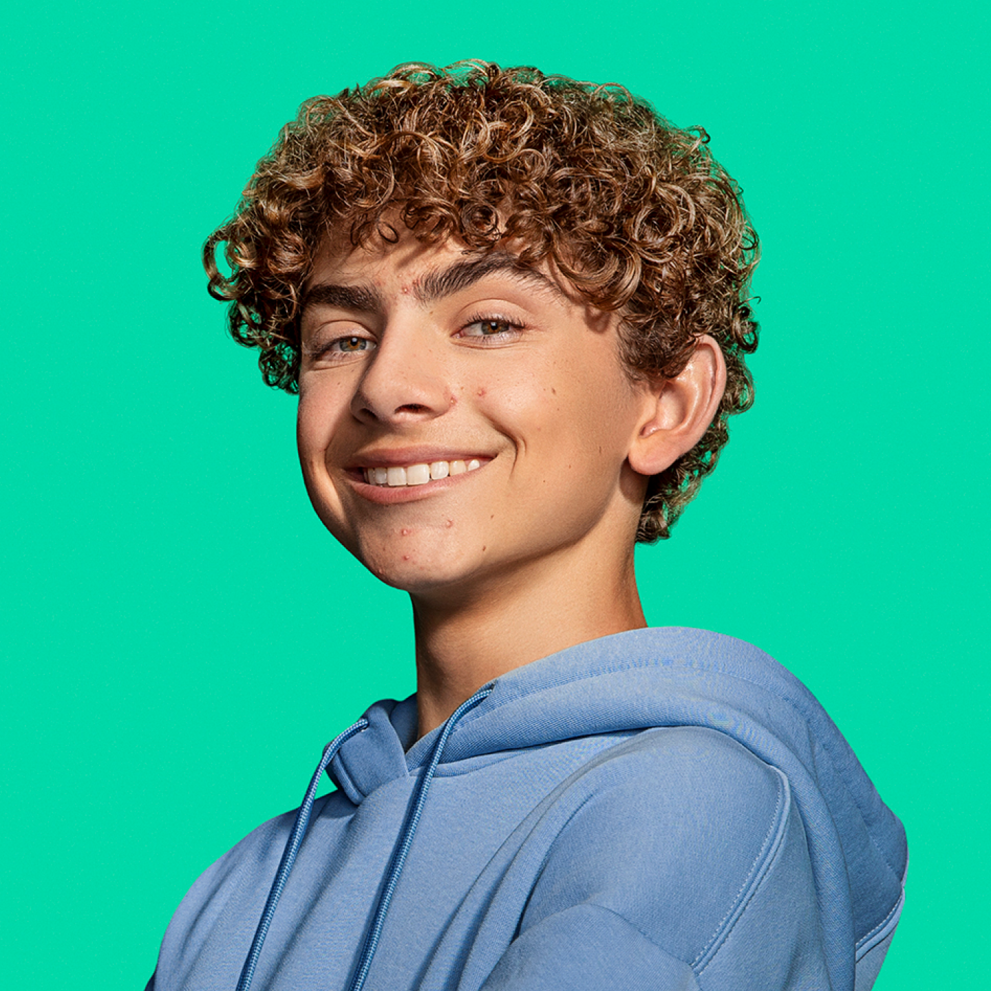 Younger male teenager with visible acne smiling confidently at camera.